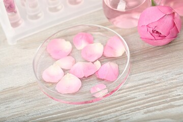 Making luxury perfume. Essential oils in glassware and flowers on white wooden table, closeup