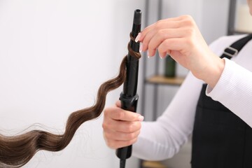 Hairdresser curling woman's hair in salon, closeup. Space for text
