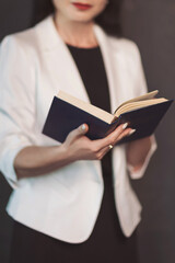 Elegant figure in a white blazer engaged in deep thought while holding an open book, illuminated...