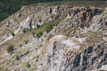 Rocky cliffside landscape showcases the beauty of nature during daylight hours near rolling hills and lush greenery in the background