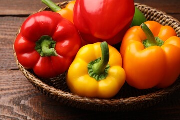Fresh colorful bell peppers in wicker basket on wooden table, closeup