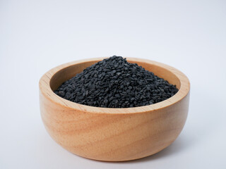 Close-up of black sesame seeds in a round wooden bowl, isolated on white background.