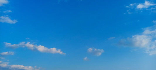 Wide panoramic view of a bright blue sky dotted with a few soft white clouds.