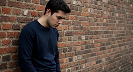 Obraz premium Young man standing against brick wall looking down in contemplation 