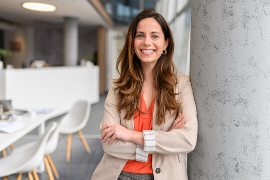 Portrait of confident female lawyer with arms crossed smiling and leaning on column in modern office