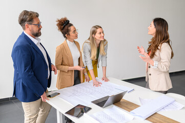 Female manager with blueprint on table discussing strategies with professional colleagues in board...