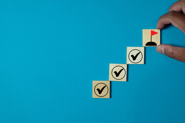 Hand placing a wooden tile with a red flag goal icon, completing steps marked with checkmarks....