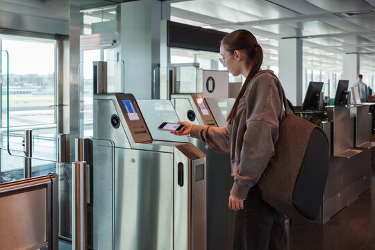 A young woman uses her smartphone to scan a boarding pass at an automated airport gate. Concept of digitalization, self-check-in and independent travel.
