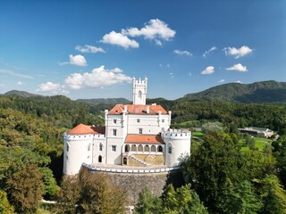 Obraz premium Trakošćan, Croatia – September 16, 2023: Aerial view of Trakošćan Castle surrounded by forested hills under a clear blue sky.