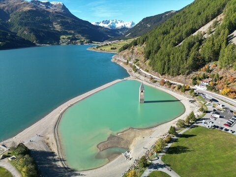 Lake Resia, Italy &ndash; October 3, 2022: Aerial view of the famous sunken church tower in the lake with turquoise water, surrounded by mountains and autumn forest near the Reschen Pass.

