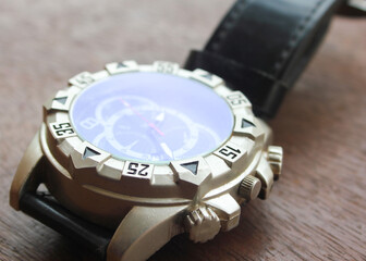 Luxury analog wristwatch with a black leather strap and stainless steel bezel, placed on a wooden...