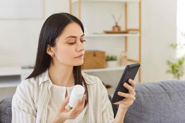 Portrait of young confident woman sitting in living room at home with a plastic bottle of medical...
