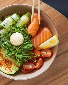A healthy poke bowl served with fresh salmon slices, cucumber ribbons, arugula, avocado, cherry tomatoes