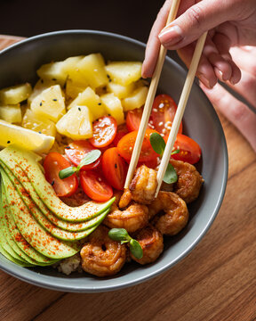 A vibrant poke bowl featuring grilled shrimp, sliced avocado, cherry tomatoes, pineapple chunks