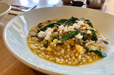A hearty and healthy dish of creamy giant couscous (or pearl couscous) prepared with chickpeas and fresh spinach, served in a modern bowl.
