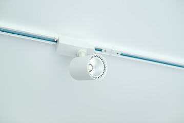 Modern white LED track light fixture mounted on ceiling rail, minimalistic interior lighting solution, close-up view.