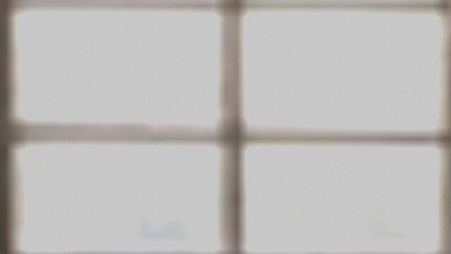 An out of focus photograph depicting a window divided into four panes by a dark frame. The view beyond is indistinct and light gray.
