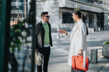 Two people engage in a friendly and professional conversation while standing in a modern urban environment under daylight, holding business bags.