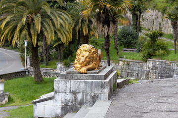 View on sculpture of a sleeping lion on a pedestal against tropical tree near entrance of Winter...