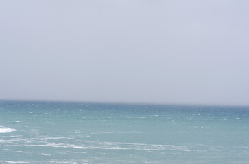Minimalistic view of a tranquil seascape with soft blue water and an overcast sky, creating a...