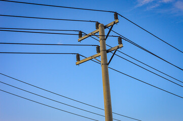 Concrete utility pole with multiple black electrical power lines against a clear blue sky