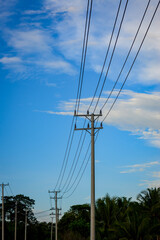 Obraz premium Utility poles with multiple power lines stretch across the image against a clear blue sky with scattered clouds