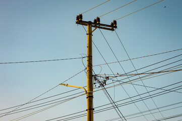 Utility pole with numerous intersecting cables set against a clear blue sky