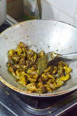 Indonesian woman cooking fish, chicken offal, potatoes in a hot frying pan