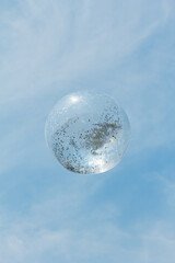 Clear bubble floating against a blue sky on a sunny day with wispy clouds
