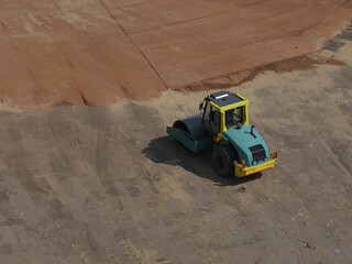 road vibratory roller compacts soil at a construction site. Top-down view. The machine leaves clear...