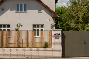 The front view of a residential house showcases an elegant gated entrance, sturdy wooden fence, and...