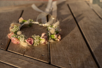 A beautiful handmade floral crown featuring roses and gypsophila lies on a rustic wooden surface. This eco-friendly accessory captures the essence of Shavuot, Wedding, Birthday festivities and nature.