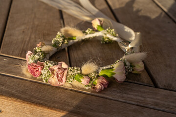 Beautiful floral crown made of roses, gypsophila, and dried wheat sits on rustic wooden surface. Perfect for Shavuot, Wedding, Birtday this handmade accessory adds touch of nature to any celebration.