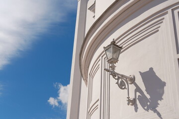 Classic street lamp casting shadow on curved white building wall. Intricate lantern attached to...