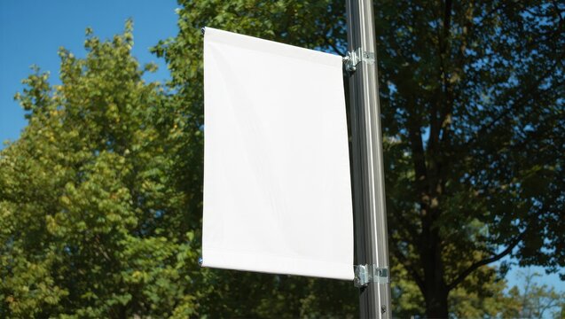 Blank white banner hanging on a pole with trees and blue sky behind
