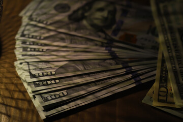 Stack of Hundred Dollar Bills Fanned Out on Wooden Surface in Low Light