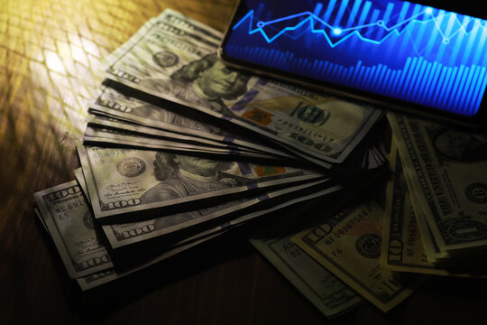 Cash and Smartphone Displaying Stock Market Graph on Wooden Table