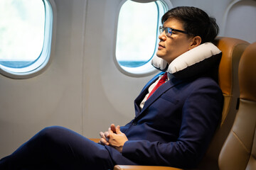 Asian business man with travel pillow sleeping in airplane during flight in first class seat