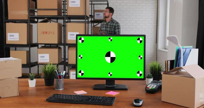 Man using desktop computer with green screen chromakey in the warehouses. A man and a woman work in a distribution warehouse full of cardboard boxes.