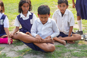 A young boy sits cross-legged in a yoga pose with focused concentration, while two classmates sit beside him