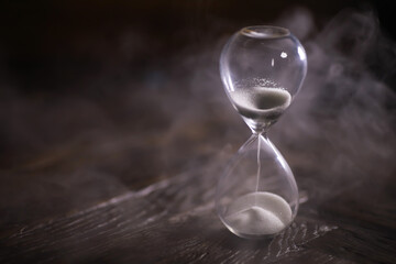 Hourglass with Flowing Sand on Wooden Surface with Misty Background