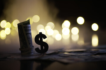 Rolled Dollar Bills and Dollar Sign Silhouette Against Blurred Bokeh Lights