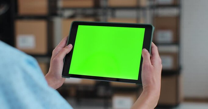 Woman using tablet computer with green screen chromakey display mockup. Browsing the Internet in a warehouse full of cardboard boxes.