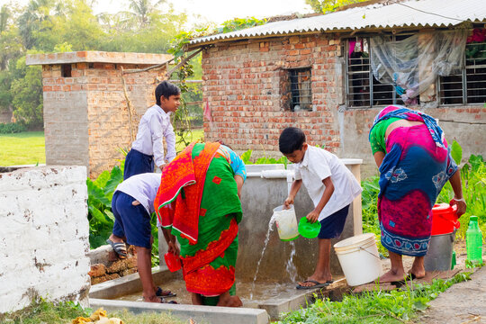 Women in colorful sarees and schoolchildren collect water together at a communal handwashing and filling station in a rural village