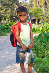 A young boy with a red backpack holding a metal lunch container and looking at the camera