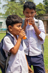 Two schoolboys in uniform enjoy chilled orange drinks under the sun, smiling and refreshed after a school day
