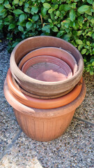 Fototapeta premium A stack of various-sized terracotta and plastic plant pots rests on a textured stone surface, backed by lush green foliage