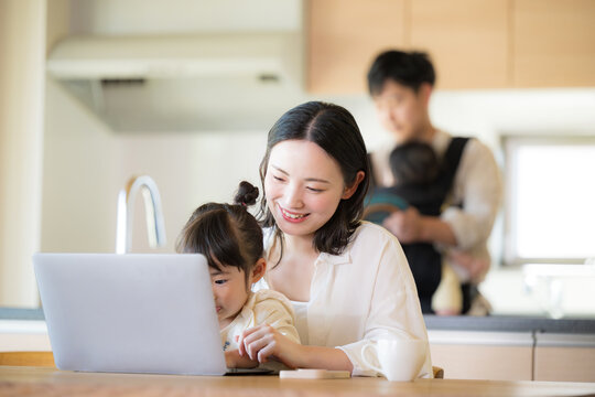 自宅のリビングで仕事をするママと家事をするパパ　リモートワーク、共働きや主夫のイメージのクローズアップ