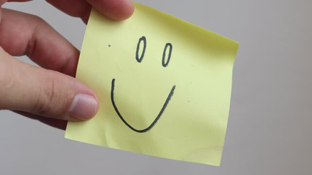 looping video: Hand holding yellow sticky note with smiley face drawing
