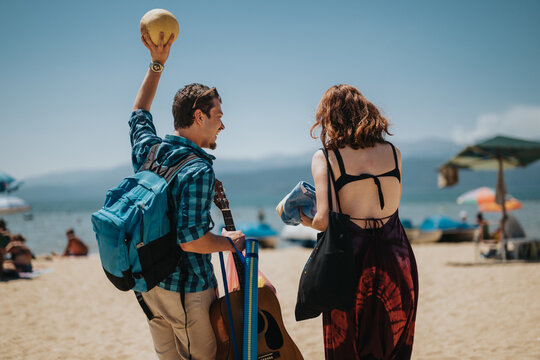 Two friends walk on a sunny beach carrying items for relaxation and fun, embodying the carefree spirit of a summer getaway.